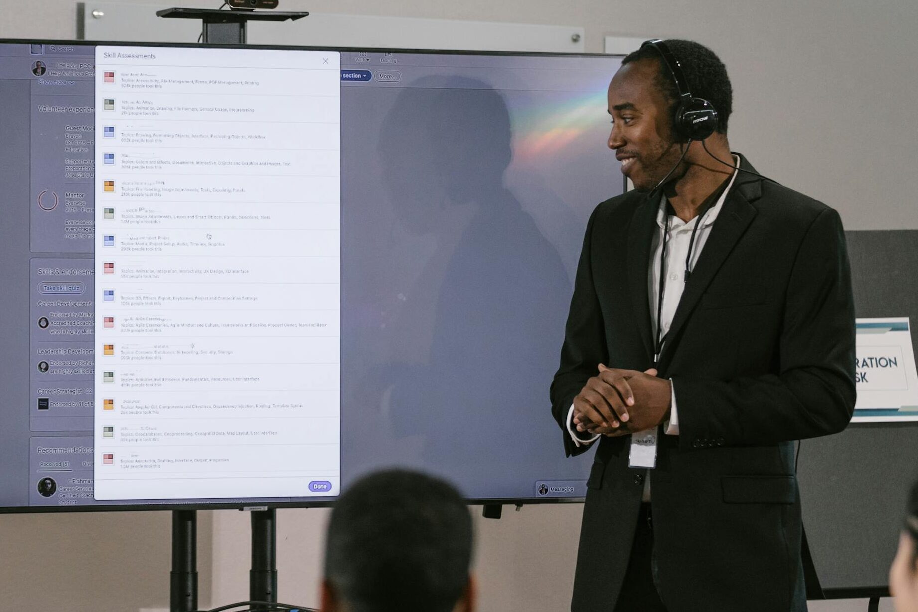 An adult man presents at a technology seminar using a large screen and headset.