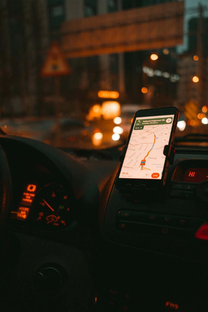 Smartphone GPS navigation on city streets at night with car dashboard in view.