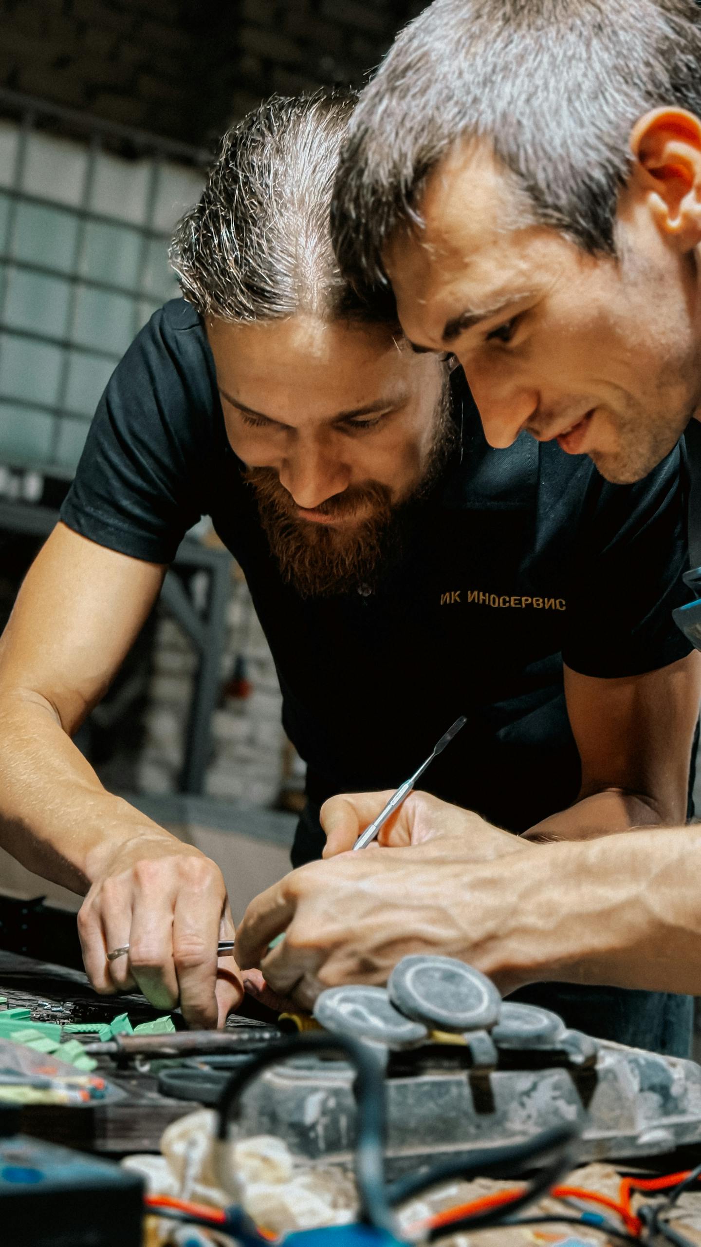 Two adults collaborating on detailed crafting work indoors, focusing closely.